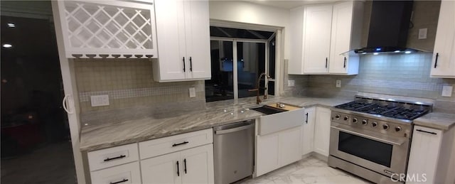 kitchen featuring appliances with stainless steel finishes, sink, white cabinets, light stone countertops, and wall chimney range hood