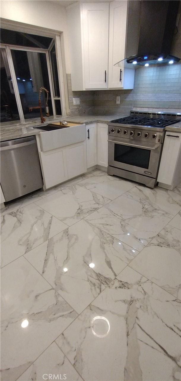 kitchen featuring wall chimney exhaust hood, sink, white cabinetry, tasteful backsplash, and stainless steel appliances