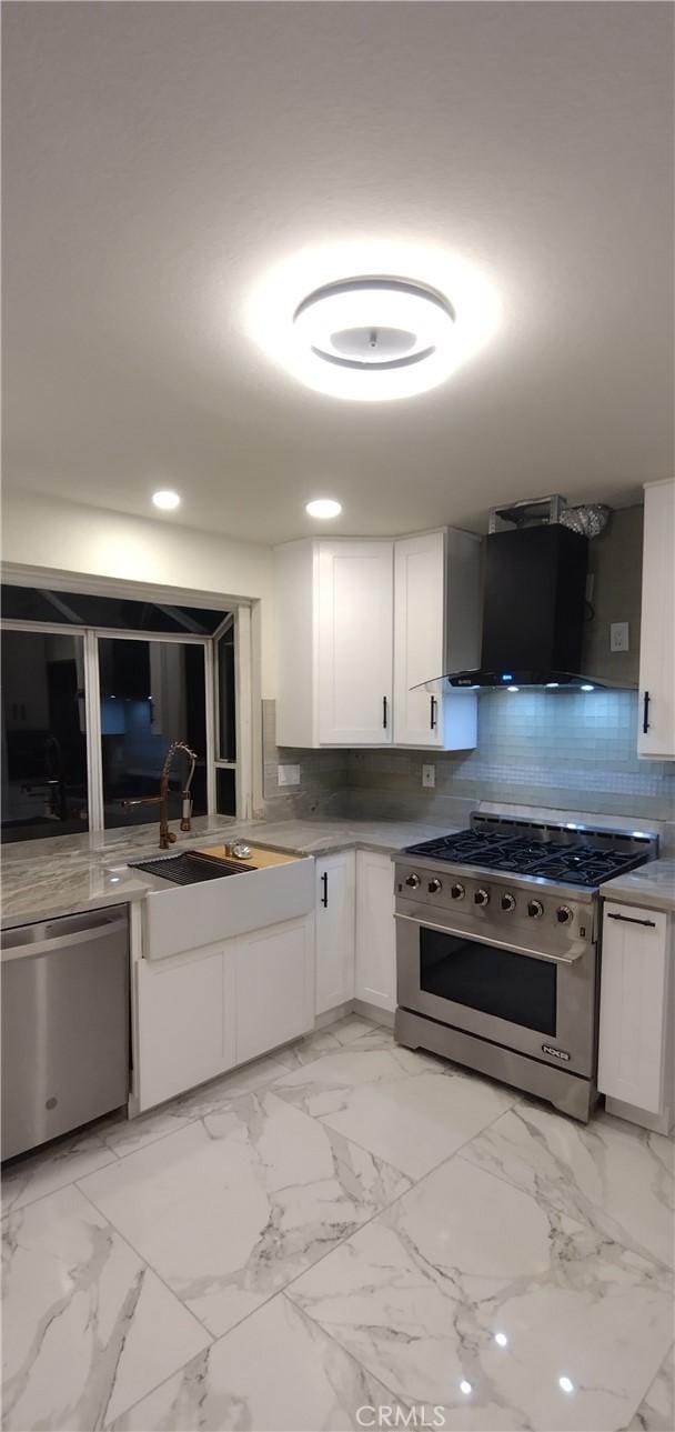 kitchen featuring wall chimney exhaust hood, sink, appliances with stainless steel finishes, white cabinets, and backsplash