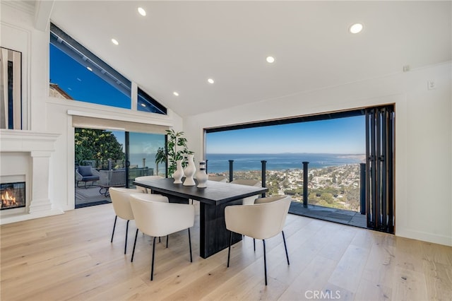 dining area with vaulted ceiling, a water view, light wood-type flooring, and a fireplace