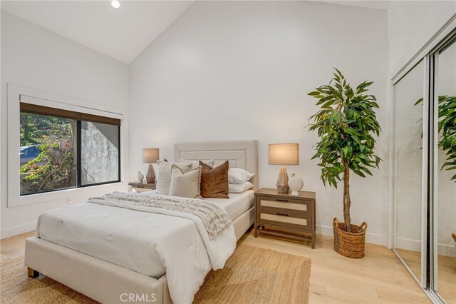 bedroom with high vaulted ceiling, light hardwood / wood-style floors, and a closet