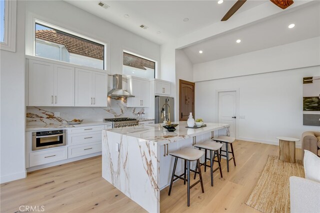 kitchen with a kitchen island with sink, white cabinets, and wall chimney exhaust hood