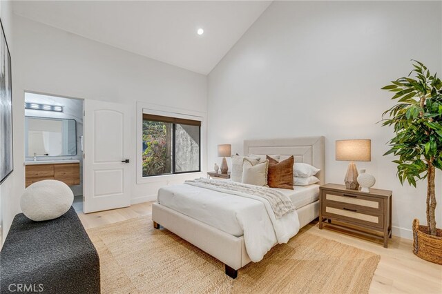 bedroom with connected bathroom, high vaulted ceiling, and hardwood / wood-style floors