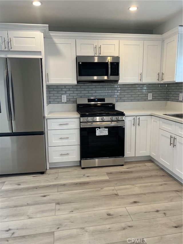 kitchen with light hardwood / wood-style floors, white cabinets, backsplash, and appliances with stainless steel finishes