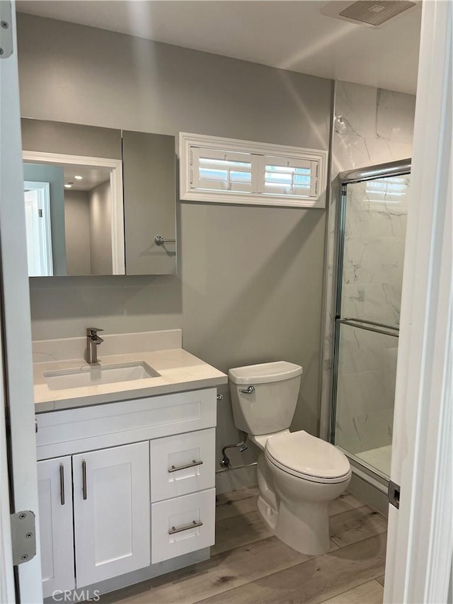 bathroom with wood-type flooring, toilet, a shower with door, and vanity