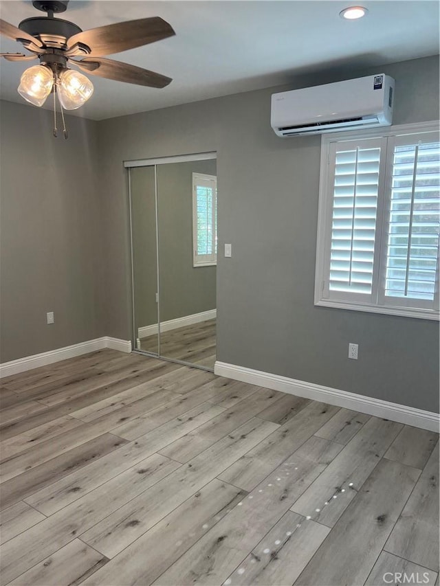 unfurnished bedroom with ceiling fan, a closet, a wall mounted AC, and light wood-type flooring