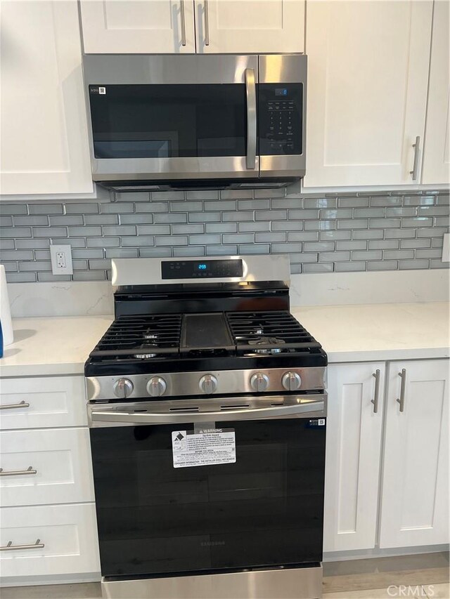 kitchen featuring stainless steel appliances, decorative backsplash, and white cabinets