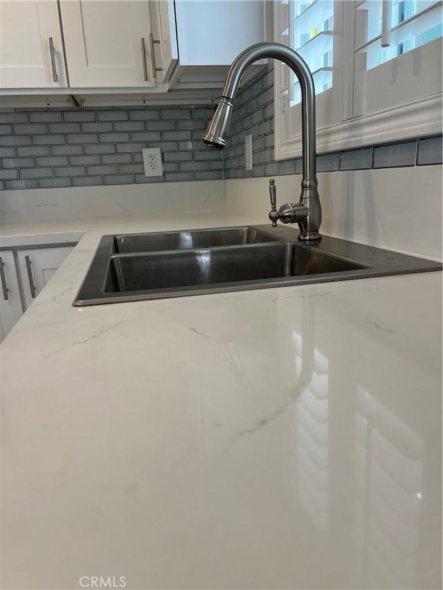 room details featuring white cabinetry, backsplash, light stone counters, and sink