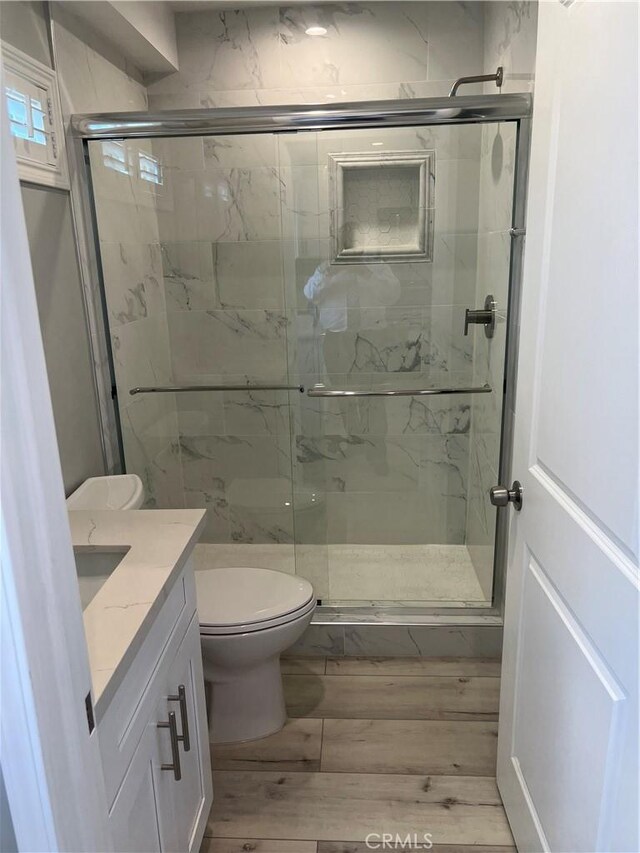 bathroom featuring hardwood / wood-style flooring, walk in shower, vanity, and toilet