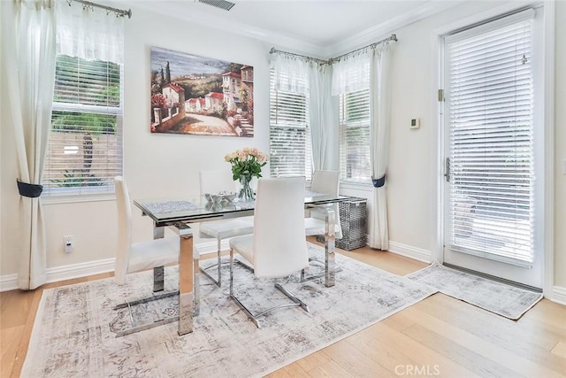 dining space with a wealth of natural light, ornamental molding, and light wood-type flooring