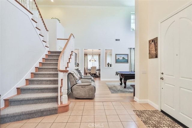 entrance foyer with light tile patterned floors, pool table, a high ceiling, ornamental molding, and a chandelier