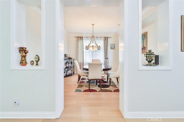 dining area with light hardwood / wood-style flooring, ornamental molding, and an inviting chandelier