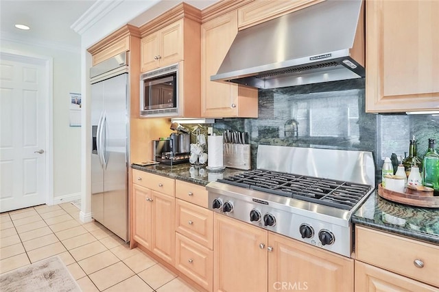 kitchen with wall chimney range hood, built in appliances, decorative backsplash, light brown cabinetry, and ornamental molding