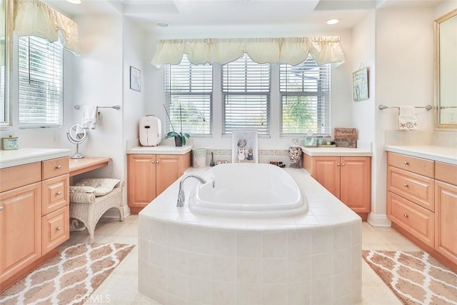 bathroom with a relaxing tiled tub, vanity, and tile patterned flooring