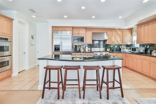 kitchen with exhaust hood, light tile patterned floors, a kitchen island with sink, and built in appliances