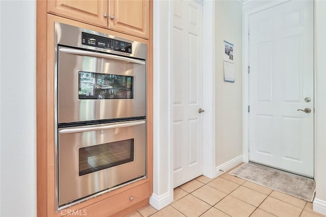 kitchen with stainless steel double oven, light brown cabinets, and light tile patterned flooring