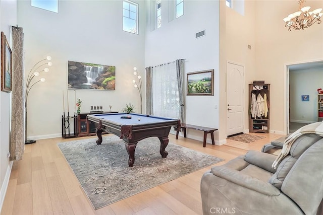 playroom with pool table, a notable chandelier, a towering ceiling, and light wood-type flooring