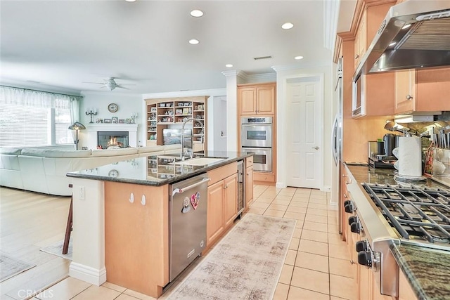 kitchen featuring appliances with stainless steel finishes, ventilation hood, ornamental molding, a kitchen island with sink, and ceiling fan