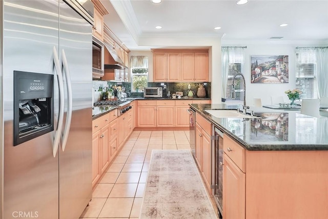 kitchen featuring an island with sink, stainless steel appliances, light brown cabinets, ornamental molding, and sink