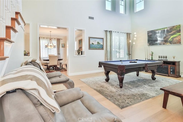 rec room with pool table, light hardwood / wood-style floors, a towering ceiling, and a notable chandelier