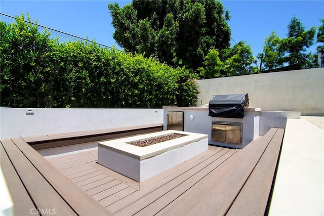 wooden terrace with grilling area, an outdoor kitchen, and a fire pit