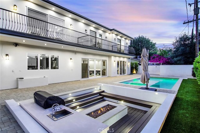 pool at dusk featuring an outdoor fire pit and a patio