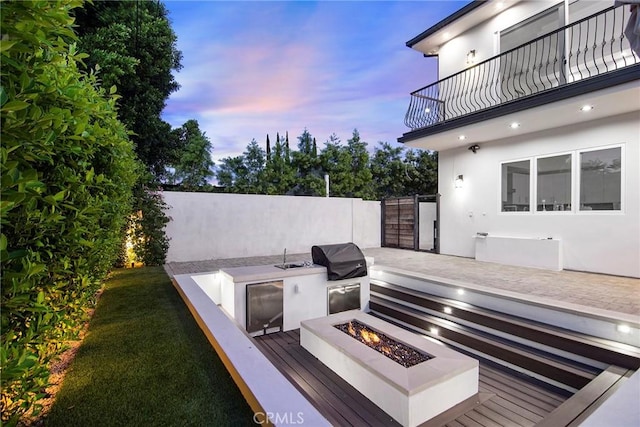 patio terrace at dusk with an outdoor fire pit, a balcony, and area for grilling