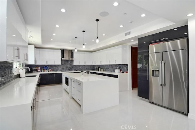 kitchen featuring decorative light fixtures, a kitchen island, a raised ceiling, white cabinetry, and stainless steel built in refrigerator