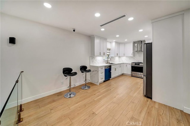 kitchen with backsplash, sink, white cabinetry, stainless steel appliances, and wall chimney exhaust hood