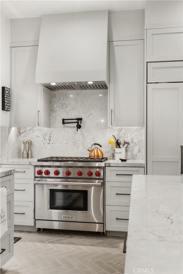 kitchen with backsplash, custom exhaust hood, white cabinetry, premium appliances, and light stone counters