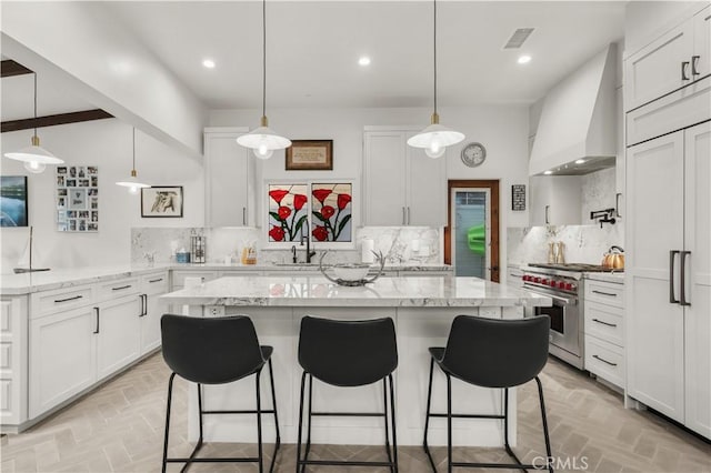 kitchen with white cabinetry, high end stove, decorative backsplash, hanging light fixtures, and custom range hood