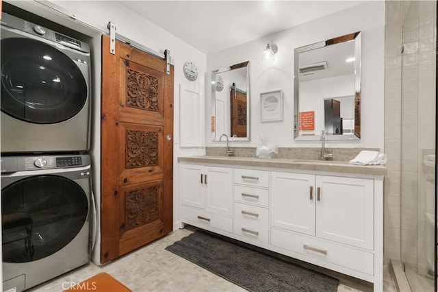 clothes washing area with sink, stacked washer / drying machine, and a barn door