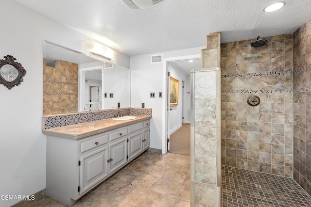 bathroom with a textured ceiling, vanity, a tile shower, and tasteful backsplash