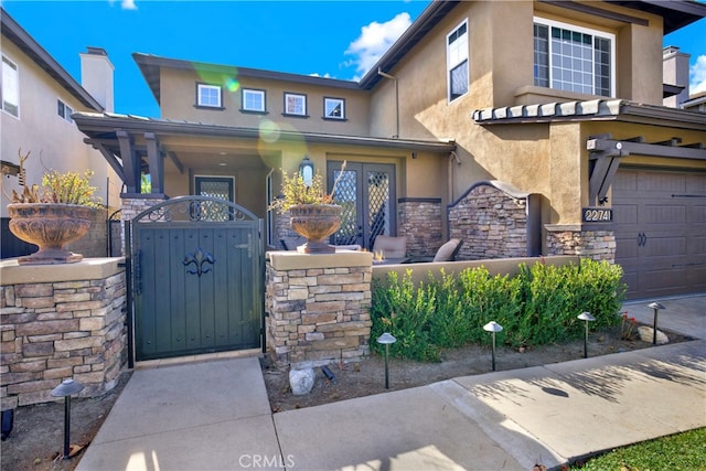 view of front facade with a garage, stone siding, a gate, and stucco siding