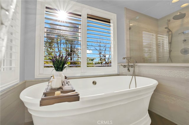 bathroom with tile walls, independent shower and bath, and a healthy amount of sunlight