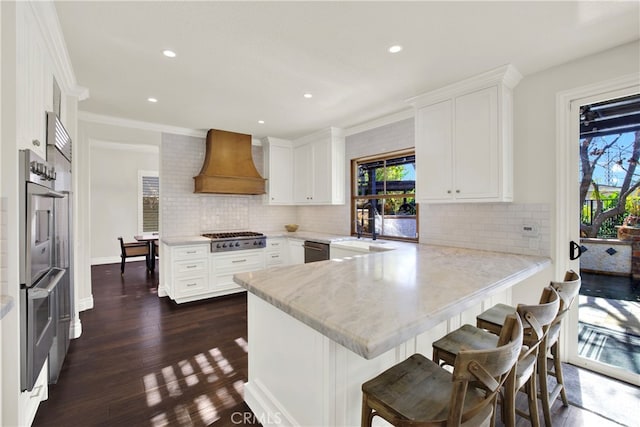 kitchen with premium range hood, white cabinets, kitchen peninsula, and appliances with stainless steel finishes