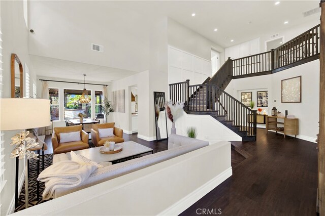 living room featuring a towering ceiling, an inviting chandelier, and dark hardwood / wood-style flooring