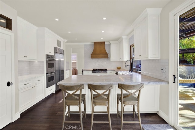 kitchen with stove, premium range hood, white cabinets, and sink