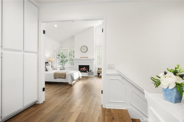 unfurnished bedroom featuring lofted ceiling, a fireplace, crown molding, and hardwood / wood-style floors