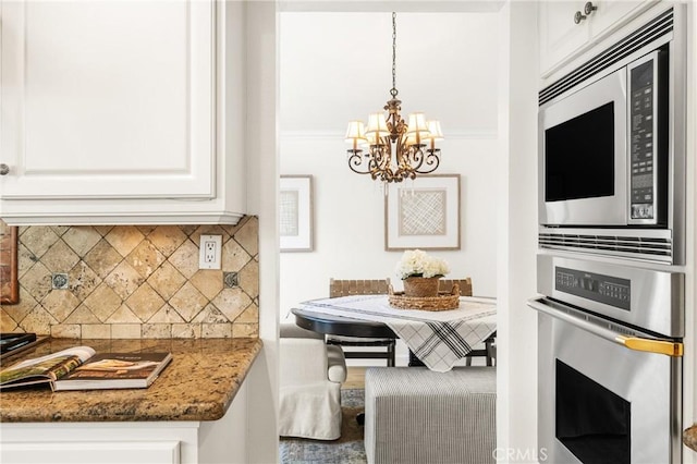 kitchen featuring a notable chandelier, dark stone countertops, white cabinetry, hanging light fixtures, and stainless steel appliances