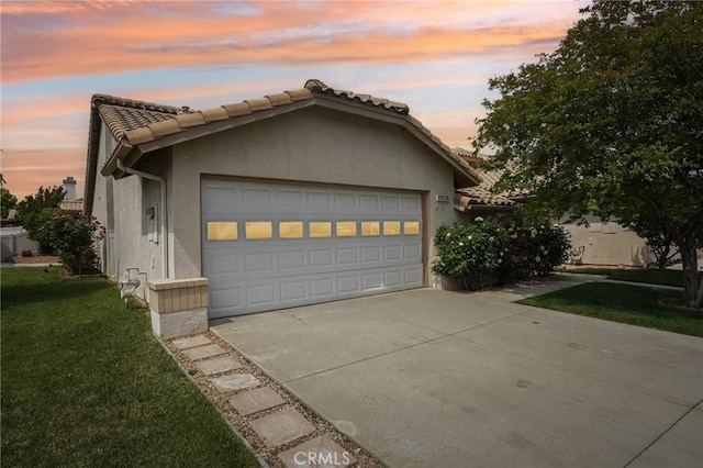 view of front facade featuring a garage, driveway, a tiled roof, a yard, and stucco siding