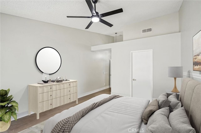 bedroom with visible vents, a textured ceiling, baseboards, and wood finished floors