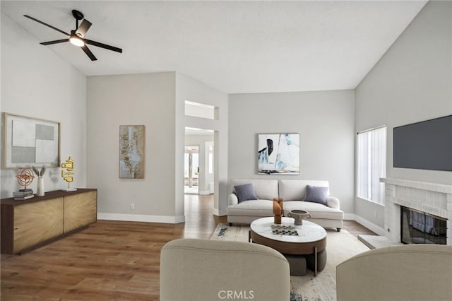 living area with a brick fireplace, a ceiling fan, baseboards, and wood finished floors