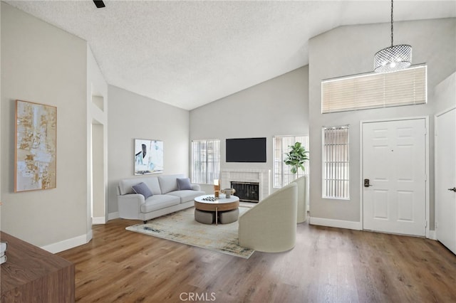 living room featuring baseboards, wood finished floors, a textured ceiling, a fireplace, and high vaulted ceiling