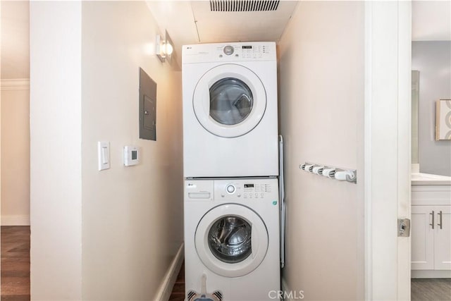 laundry room with wood-type flooring, stacked washer and clothes dryer, and electric panel