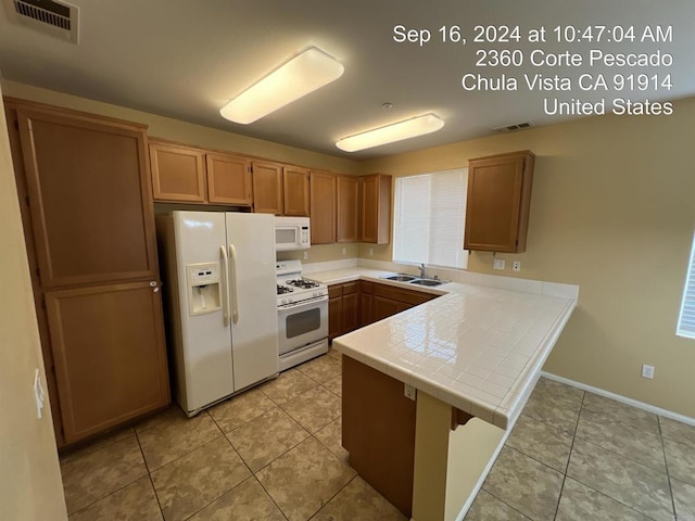 kitchen with tile countertops, sink, light tile patterned floors, kitchen peninsula, and white appliances