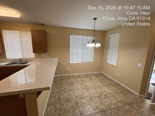 kitchen with sink, hanging light fixtures, tile counters, kitchen peninsula, and an inviting chandelier