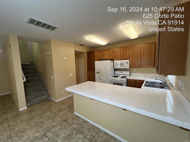 kitchen with sink, light tile patterned floors, tile counters, kitchen peninsula, and white appliances