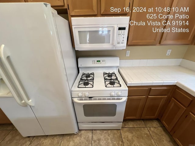 kitchen featuring light tile patterned flooring, white appliances, and tile countertops