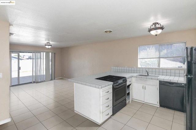 kitchen with kitchen peninsula, tile counters, white cabinets, and black appliances